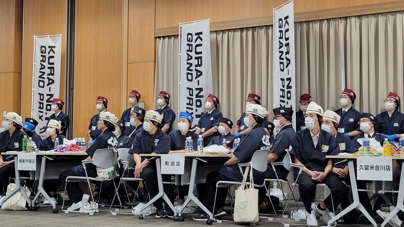 今回の「KURA-No.1 GRAND PRIX」の舞台は、くら寿司大阪の貝塚事務所。国内外24店舗のスタッフが一堂に会し、会場は賑わいながらも、少しピリッとした緊張感が漂っていました
