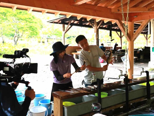 教わりながら、ニジマスを串に刺していく。©釣りビジョン