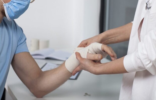 手首に包帯を巻いてもらうマスク姿の男性