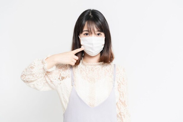 白い背景の前に立っている、マスクをした若い女性