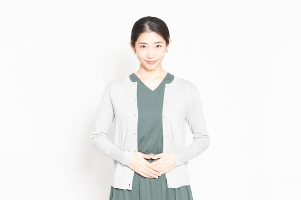 白背景の前に立って、お腹に手を当てる女性