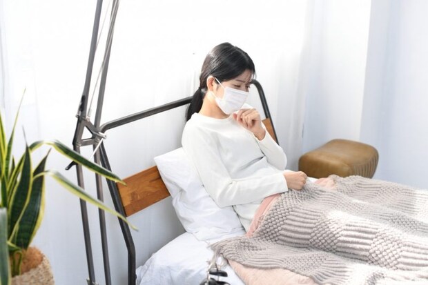 ベッドで咳をする体調不良のアジア人女性