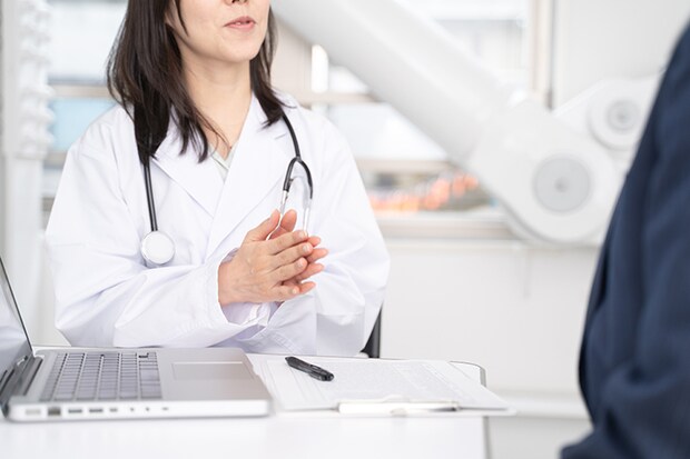 ノートパソコンを見ながら病状を説明する女医と男性患者の手元