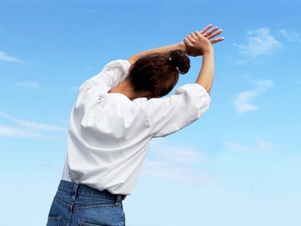 手首を持って体を横に伸ばす女性_青空