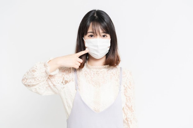 白い背景の前に立っている、マスクをした若い女性