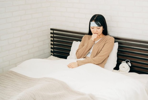 ベッドで休む体調不良の女性（冷却シート・咳）