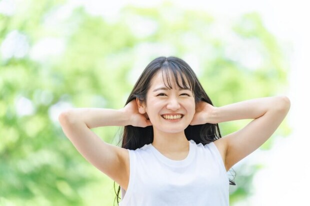 新緑の中で髪を触る笑顔の日本人女性