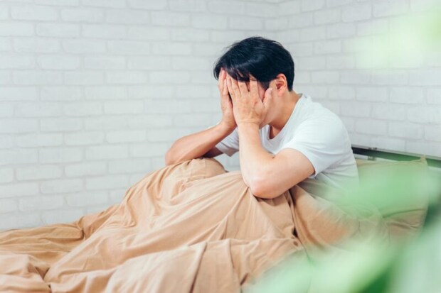 ベッドで顔を覆う男性