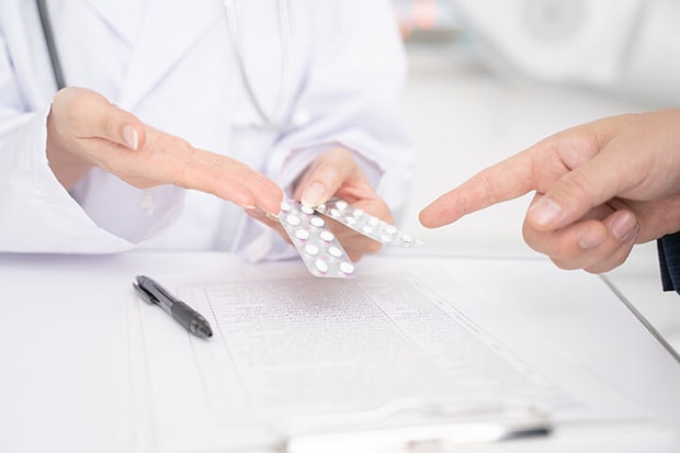 処方薬の説明をする女医と男性患者の手元