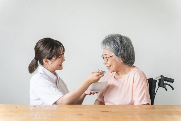 食事する高齢者女性と食事介助する介護士