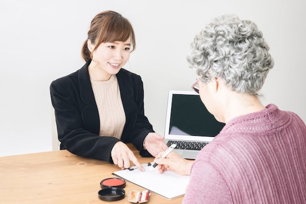 スーツ姿の女性と書類にサインする高齢者