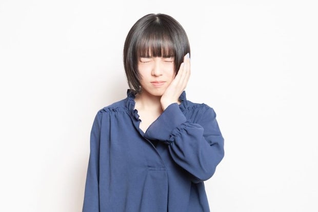 歯が痛くて頬に手を当てる若い女性
