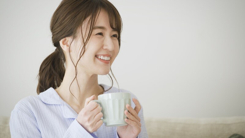マグカップを手に持ち、にっこりする女性