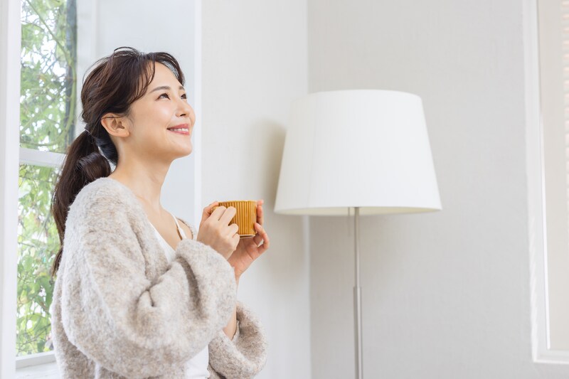 マグカップを手に持ち、部屋でホッとする女性