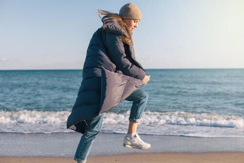 ダウンコートを着て海辺を歩く女性