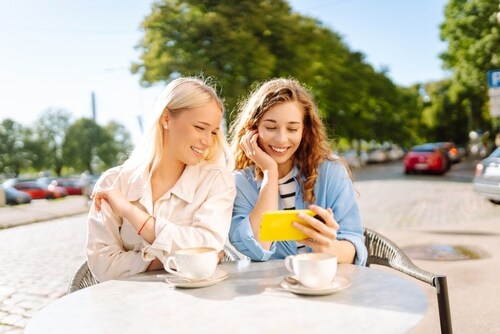 カフェでスマートフォンを見ながら楽しそうに話す女性達
