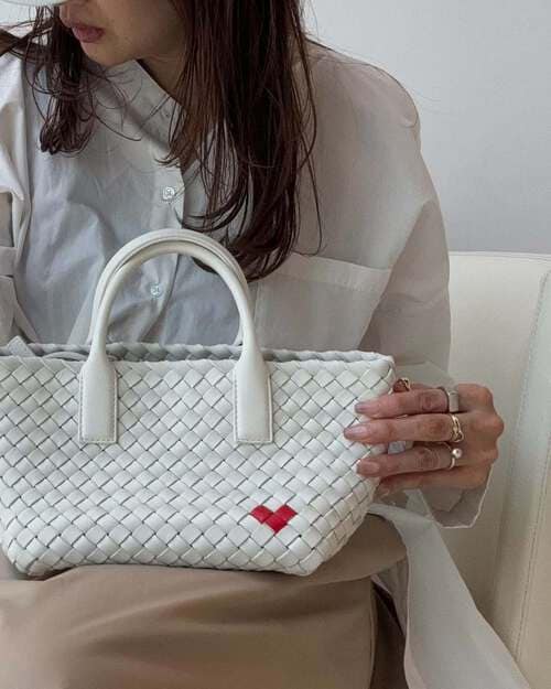 ボッテガのホワイトのバッグを膝に乗せて座る女性