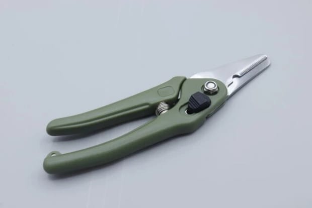 グリーンのグリップと銀色の刃のダイソー園芸万能ハサミが開いた状態で置かれている