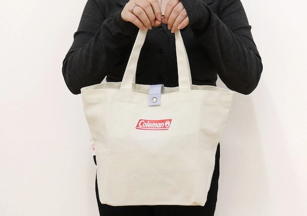 黒い服を着た女性がColemanロゴ入りナチュラルカラートートバッグを両手で持っている着用イメージ