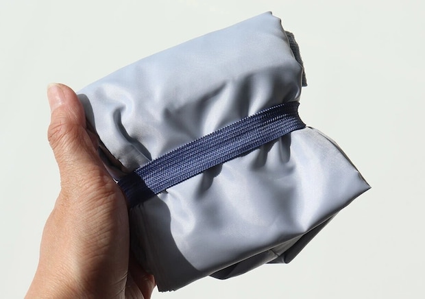 コールマンのライトブルートートバッグをゴムバンドで小さくまとめた状態を片手で持っているコンパクト収納写真