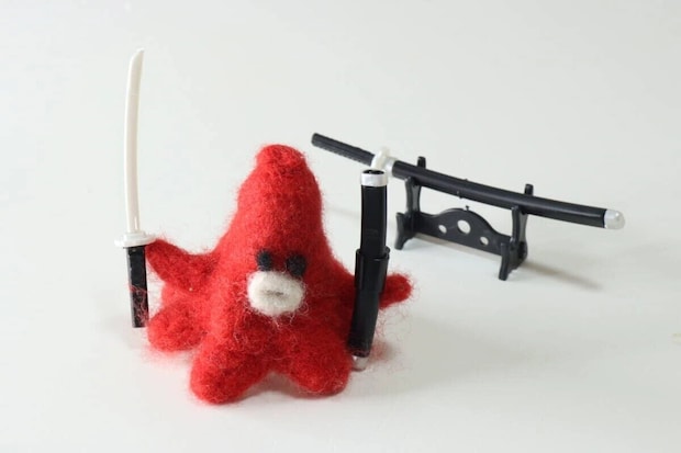 赤いぬいぐるみに白い長刀を持たせ刀掛けに飾った刀を並べた写真