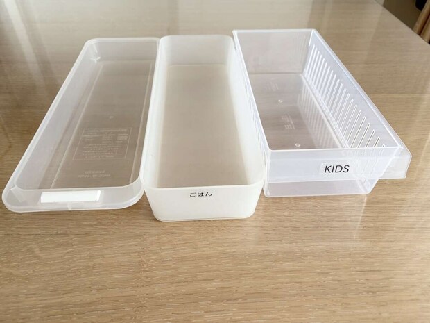 木のテーブルに並べられた透明と半透明の収納ケース3点（「ごはん」「KIDS」のラベル付き）