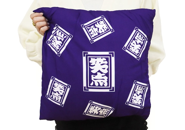 白いニットの女性が笑点座布団クッションを抱きかかえている様子