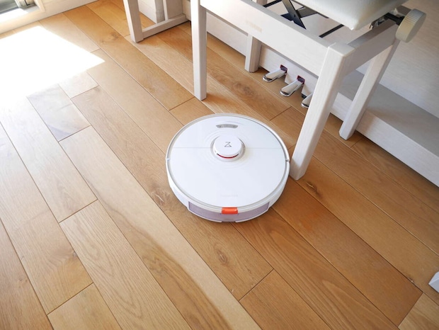 無垢材フローリングの上で稼働している白いロボット掃除機
