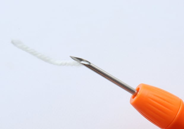 スレダーを使ってニードルペンに白い毛糸を通している様子
