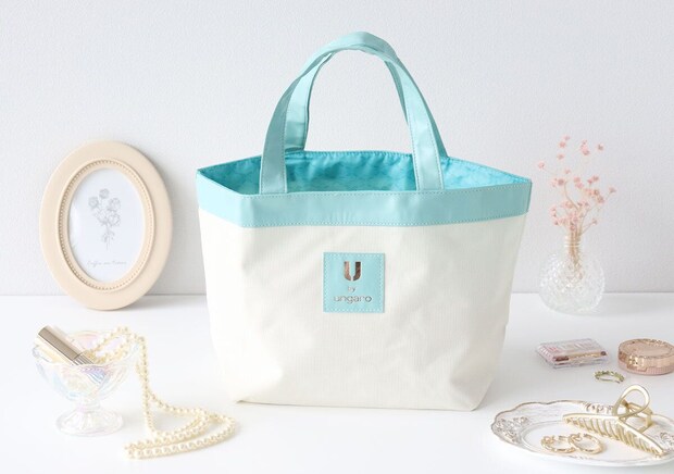 U by ungaro 舟形トートバッグと小物の俯瞰写真 白い壁の前に置かれた舟形トートバッグと、額縁・パールネックレス・ドライフラワー・アクセサリーなどを並べた俯瞰写真