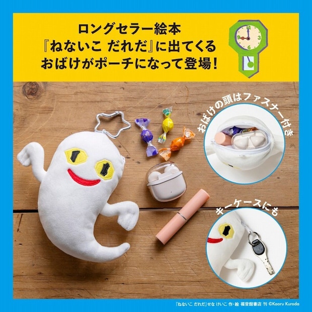 木目の床の上で、星形カラビナを付けた黄色い目と赤い口の白いおばけぬいぐるみポーチが横たわり、隣に包み紙キャンディとAirPodsケース、ピンクのリップが並ぶ俯瞰写真