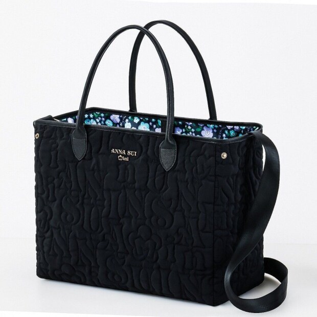 ANNA SUI miniの黒いロゴキルティングのビッグトートバッグ。黒い持ち手とショルダーストラップ、アンティークゴールドのロゴプレートが付き、内側はパープルとブルーの花柄プリント