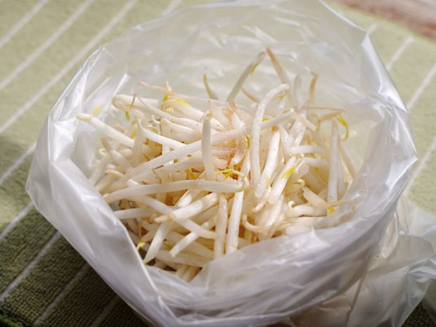 透明なビニール袋に入れた生のもやし。緑のストライプの布の上に置かれている
