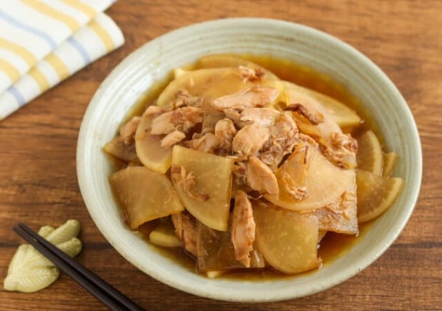 器に盛ったツナ大根(大根とツナの煮物) いちょう切りの大根とほぐしたツナを煮たツナ大根を、淡い緑色の器に盛り付けた写真。木のテーブルに黒い箸と練りからしが添えられている