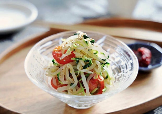 ガラスの器に盛られたもやしと豆苗のナムル。半分に切ったプチトマトと白ごまがのり、木のトレイにのっている