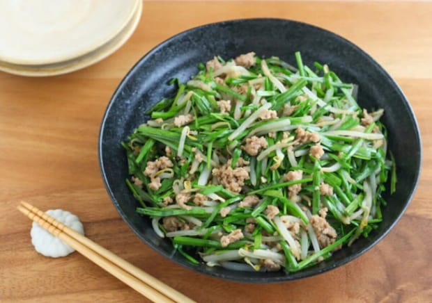 黒い器に盛ったニラもやしと豚ひき肉の炒め風 黒い器に盛られたニラ・もやし・豚ひき肉の炒め風。緑のニラがたっぷりで木のテーブルに箸が添えられている