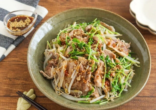 緑色の和食器に盛られた豚うす切り肉ともやし、豆苗のレンジ蒸し。白ごま入りのピリ辛中華ダレがかかっている