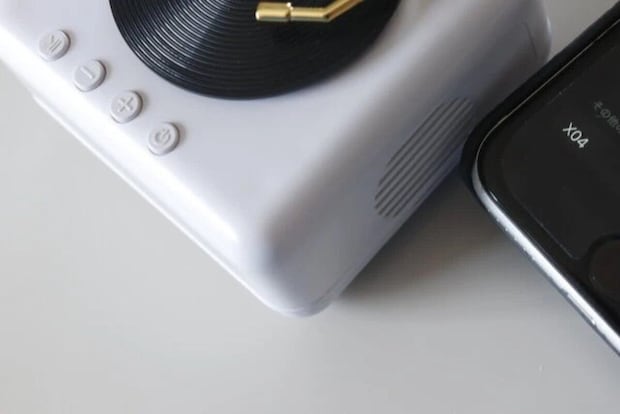 白いレコードプレーヤー型スピーカーの横にスマートフォンが置かれ、Bluetooth接続画面が見える