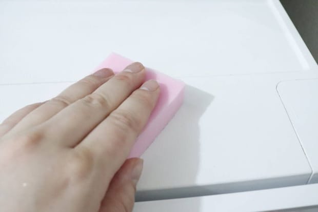 ピンクのメラミンスポンジで冷蔵庫上を掃除する手 ピンクのメラミンスポンジで冷蔵庫上を掃除する手