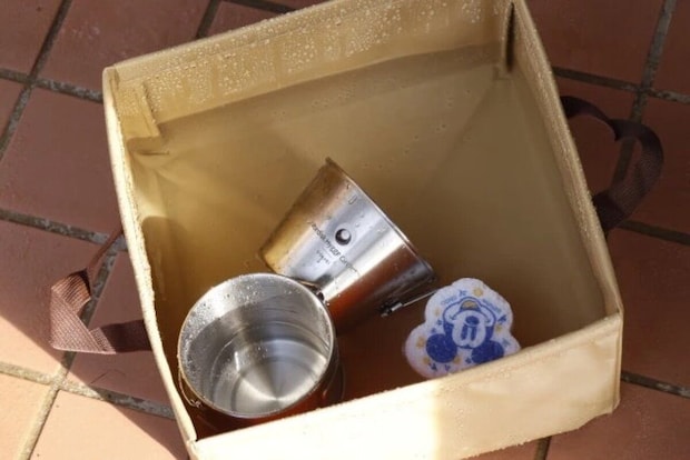 水と食器が入ったベージュ色の折りたたみキャンプバケツ 水と食器が入ったベージュ色の折りたたみキャンプバケツ