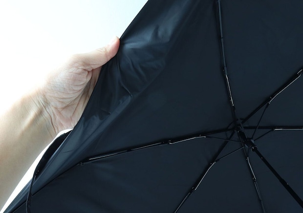 開いた黒い日傘の内側を、手がめくり生地の厚みと骨組みを見せている 開いた黒い日傘の内側を、手がめくり生地の厚みと骨組みを見せている