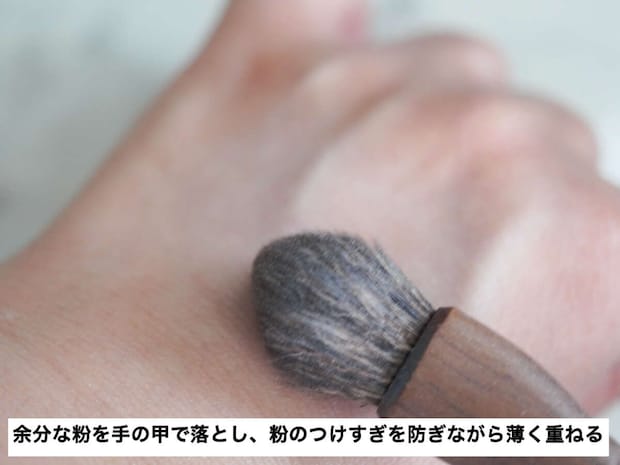 フェイスパウダーを含ませたブラシの余分な粉を手の甲で落とす様子