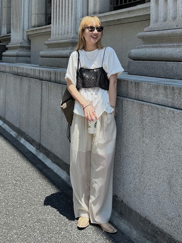白Tとベージュパンツに黒ビスチェを重ね着しコーヒーを持つ女性