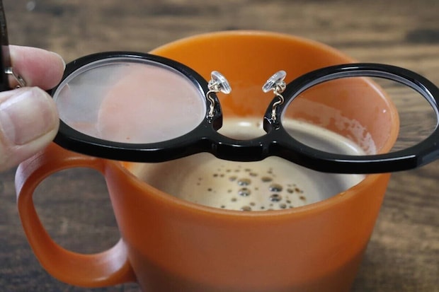 黒縁メガネを湯気の立つホットコーヒーのカップにかざしている様子 黒縁メガネを湯気の立つホットコーヒーのカップにかざしている様子