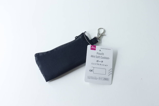 白い背景に置かれた黒いミニポーチ。商品タグが付いている。