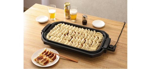 ホットプレートでたくさんの餃子が焼かれ、手前には焼き餃子とビール