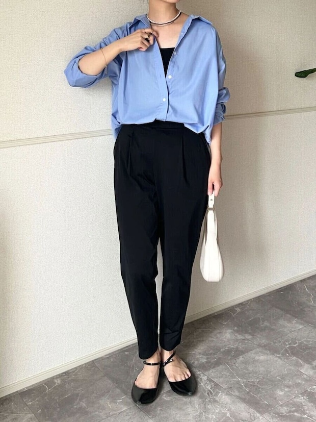 黒いテーパードパンツと水色シャツを着た女性