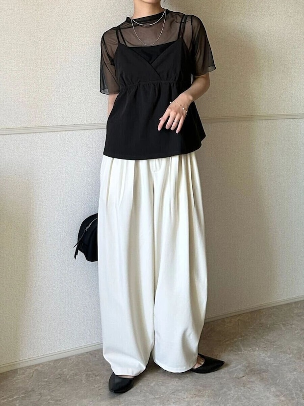 黒いシアーTとキャミソール、白いワイドパンツを着用した女性の全身