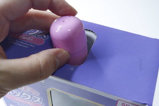 ガチャガチャボックス上部の穴からピンクのカプセルを戻している手元