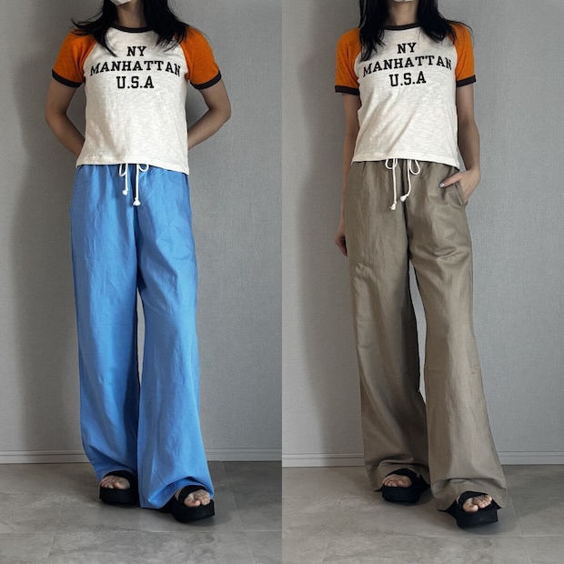 白とオレンジのロゴTシャツとブルー・ベージュパンツを履いた女性
